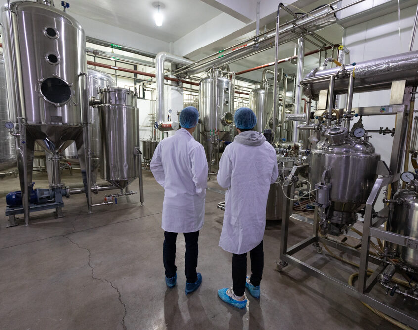 Two people in white coats standing in a factory conducting a report.