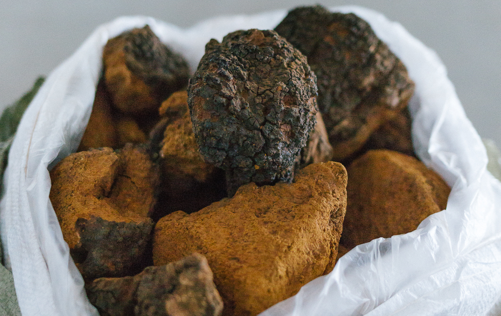 A basket filled with large organic black truffles, viewed up close. The truffles have a rough, uneven texture and are nestled in a white liner.